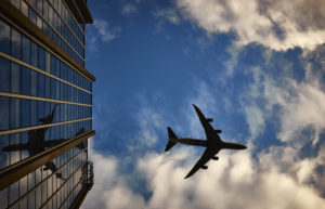 A plane flying over a building taking people to vegan travel destinations